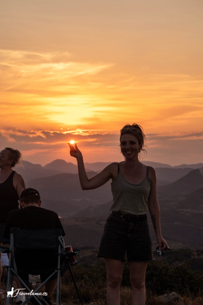 Jeune femme de profil qui désigne le soleil couchant au-dessus des montagnes