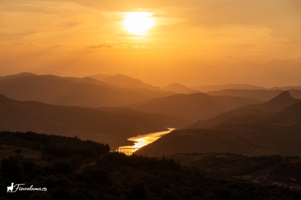 Soleil couchant sur des montagnes, rivière réfléchissant la lumière au fond de la vallée