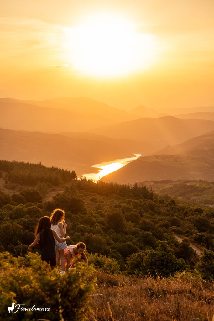 Deux personnes assises dans la garrigue regardant le soleil se coucher sur une vallée