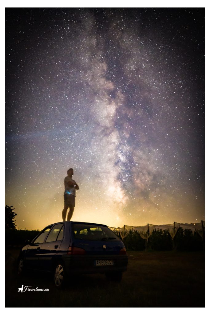Voie lactée dans un ciel étoilé au-dessus d'une personne debout sur le toit d'une voiture