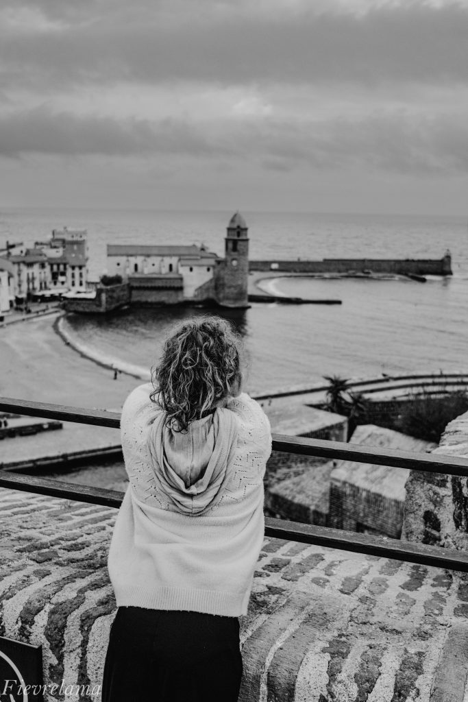 Jeune femme de dos regardant le port de Collioure et ses barques, photographie en noir et blanc